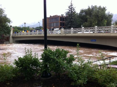 Boulder Creek rising under a bridge in downtown Boulder. Deep beneath the floodwaters are multiple lanes of bike and walking paths and a tall scenic waterfall.
