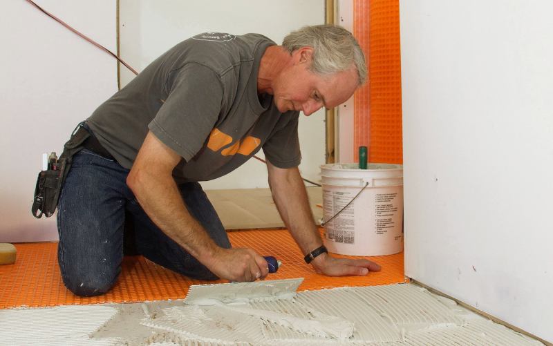 Tile contractor Tom Boucher of Integrity Tile, based in Kennebunk, Maine,  applies latex-modified Bostik Ditra-Set mortar to an Advantech subfloor to make a mortar bed for adhering Schluter Ditra decoupling underlayment membrane for a custom marble tile floor in a bathroom for a new house under construction next to the ocean south of Portland, Maine.