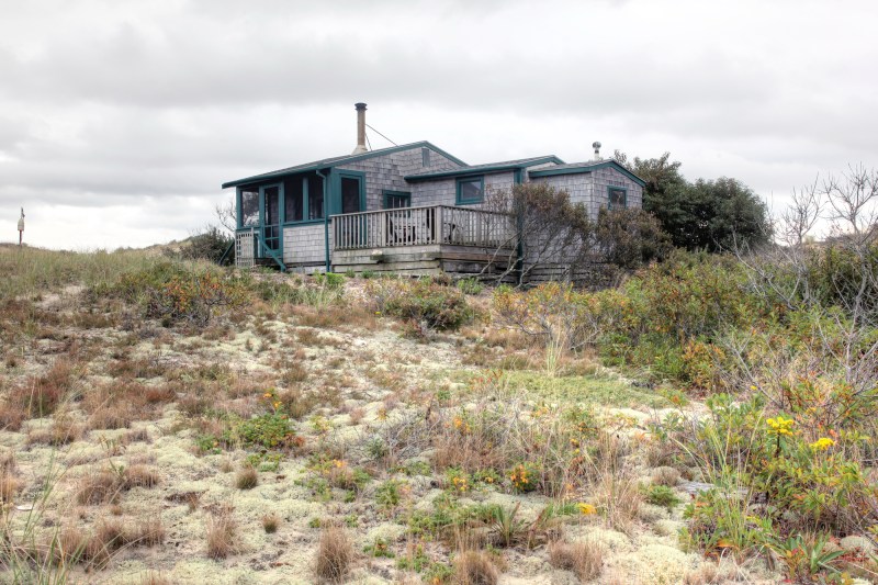 A view of the dune shack showing the main volume of the house stepping down to the bedroom and toilet room. Exterior deck is accessed from the screen porch.