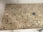 Irregular stone pebbles add a natural design element to a tiled shower but should be installed over a base with more pitch than normal to allow for better drainage. For ease of application, a good sanded high-performance grout rather than epoxy grout is recommended for use with natural stone pebbles.