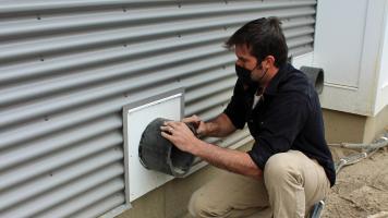 Eric Hartman of Harvestar, in Lincoln, Vt., gets ready to install the grille on the ERV exhaust outlet. The fresh-air intake is behind him. The manufacturer (and building codes) require that the outdoor air intake and exhaust air grilles be located a minimum of 10 feet from each other