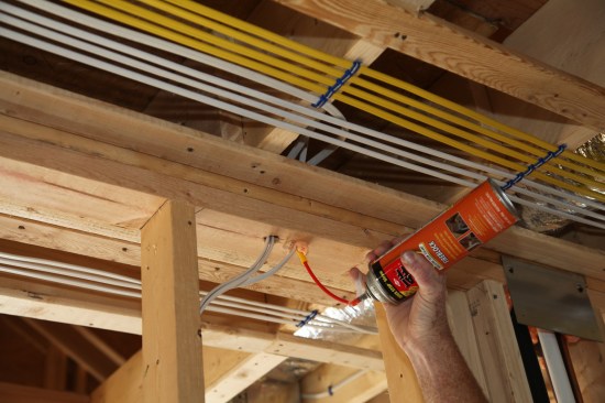 To finish the rough-in work, a crew member fills every penetration between floors with fire-resistant expanding foam to insulate against air movement and to help impede the potential spread of fire in the stud bays.