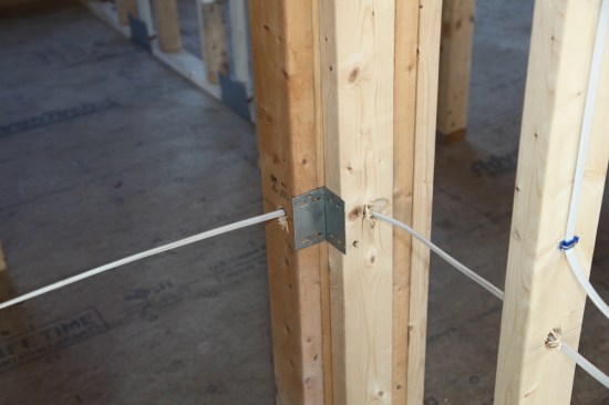 If the cable is within 1 1/4 inches of the stud surface, metal plates are required to prevent damage from errant drywall screws. Here, the angled hole to route
a cable a round a corner is too near the surface, so metal plates protect the cable on both sides of the corner.