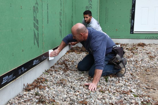 A plastic spreader is a great way to create the initial bond of the tape to the sheathing. If enough pressure is carefully and meticulously applied, the spreader can create the permanent bond. Whenever possible it is always best to go over the tape with a roller.