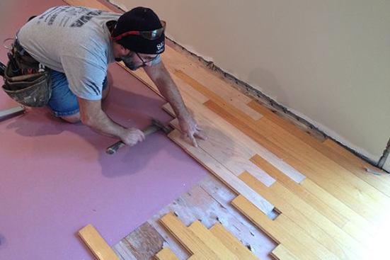 Using a block to protect the end of the board, Manny taps on the end of the new board until it hits home against the existing board.