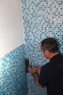 First slice through the mesh backing with a razor knife. Then slide a row (or rows) of tiles over with a flat taping knife until an acceptable groutspace is left along the corner.