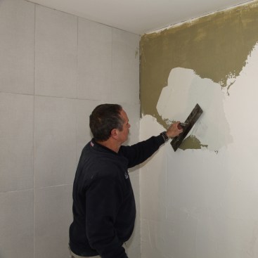 Wall prep for a glass-tile installation begins with a coating
of a liquid stress-crack membrane (the dark tan layer). Then add a coating of glass tile mortar over that.