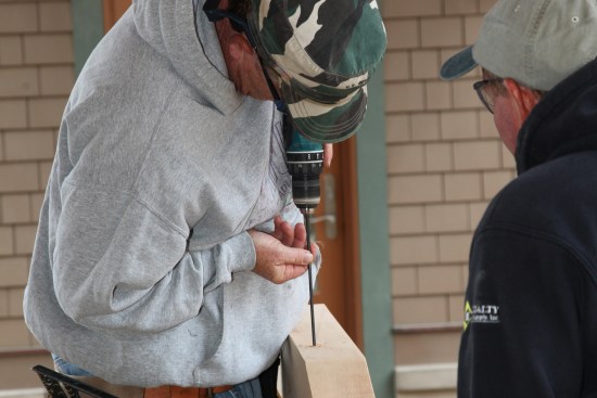 A crew member carefully drills  slightly over-size holes for the screws. A Forstner bit creates pockets for the screw head on the top side of the beam.