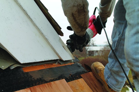 The flashing behind this rake trim needed to be replaced, so a crew member uses a recip saw with a long blade to clip the nails holding the original  flashing in place.