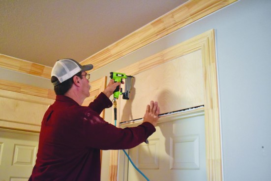 After extending the door trim to include the transom area, the crew member removes the drywall and installs a plywood panel.
