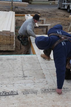 When snapping the line, the crew member in the foreground holds one end of the chalk line on the mark. The other crew member extends the line through the corner mark to the end of the house. Holding the line in place with a boot means only the line in the area of the wall is snapped.