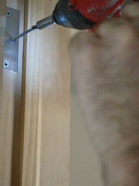 When you are happy with the hinge jamb, remove one of the hinge screws and replace it with a screw long enough to screw into the framing behind the jamb. The screw secures the top hinge in place for the rest of the installation.