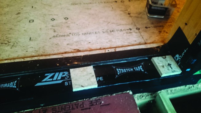 At the doorways, the crew held the top layer of sheathing back 5 inches. Flexible flashing tape laps onto the second layer of subfloor, forming a waterproof sill pan for each door.