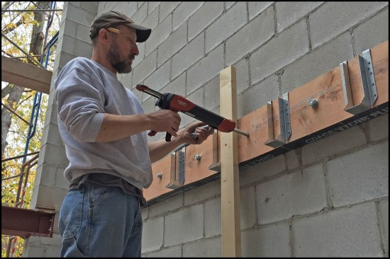 3x10 ledgers (with pre-installed joist hangers) were anchored to the wall’s floor-level bond beams. Prior to lifting and securing the 3x10 ledgers in place, peel-and-stick membrane was applied to the back of the ledger and holes were pre-drilled at the expansion bolt locations. While the ledger was temporarily held in place with 2x4 bracing, Hilti HIT-HY 70 two-component epoxy was injected into the holes using a Hilti HDM 500 manual dispenser gun. An expansion bolt was inserted and then tightened it down. After a little while, the epoxy cured and the anchor connections were rock hard.