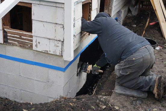 To finish the exterior of the new foundation, the crew applied waterproofing to the block, after first masking off the part of the block wall that would extend above grade.