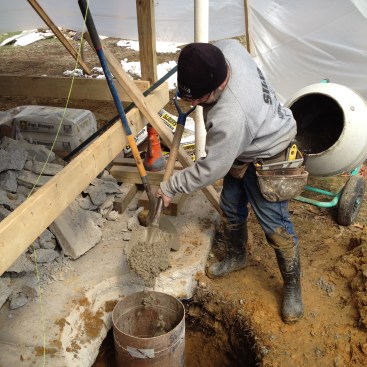 Concrete for the footing is mixed and shoveled into each form. The bottom of the footing where it was wet received a stiffer batch of concrete.