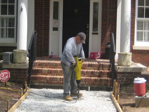 Prep work begins with installing a concrete slab to serve as a foundation for the brick walkway. The author excavates down about 8 inches and compacts the subsoil before placing 4 inches of washed gravel. Next, he sets the forms for the concrete and compacts the gravel layer with a mechanical compactor. 