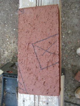 The author places the template on a brick, lining up the piece of aluminum angle with the line drawn on the template and marking the other side of the angle to lay out the exact shape that needs to be cut out. A 4 1/2-inch grinder with a diamond blade makes fast work of odd-shaped cuts such as this one.