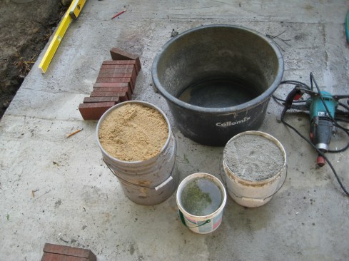 The recipe for brick-laying mortar is two-and-a-half parts masonry sand to one part Type-S masonry cement plus water. After combining the sand and the water together in a mixing tub, the author mixes in the masonry cement, stirring the mortar with a mixing paddle on a heavy-duty drill. When it’s thoroughly mixed, he slowly adds water until the consistency is right. 