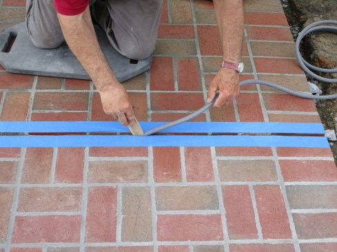 The final step is filling the brick joints over the control joints in the concrete slab. The author tapes the edges of the bricks, pushes foam backer rod into the joint.