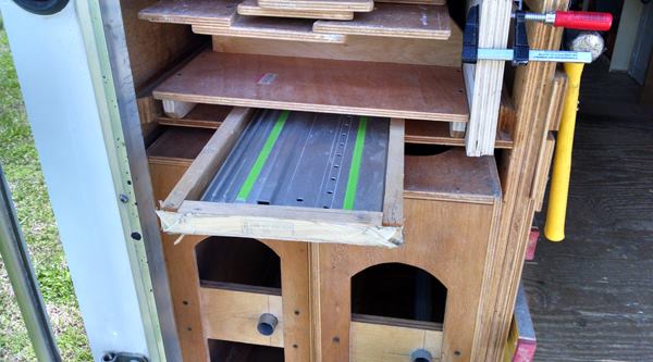 The Workbench II stores in a long opening at the left rear end of the trailer. The pair of “box beams” that make up the top can be seen at the bottom of this photo. Other parts store above. This area is also used for storing track saw guide rails.