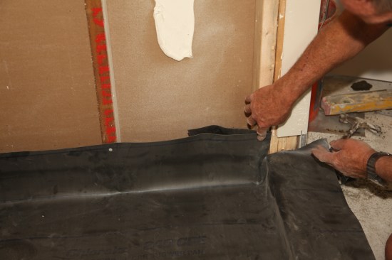 The membrane needs to be cut where it transitions from the vertical plane of the walls to the horizontal plane of the threshold. This area demands close attention to keep it waterproof. The first step is to cut the membrane tight to where the top of the threshold meets the jamb framing, allowing the membrane to wrap over the top of the threshold.