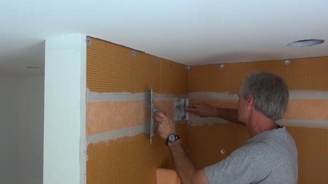 Boucher presses the Kerdi-Band into the mortar with the flat edge of the trowel. When the ridges from the notched trowel are no longer visible through the translucent membrane, a good bond is assured.