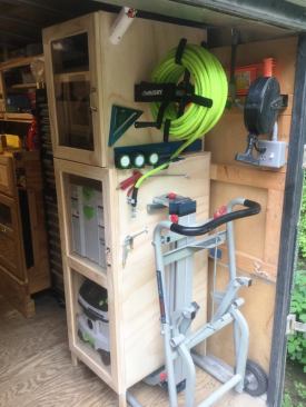Air is supplied to the hose reel by the copper line that runs from the compressor seen in an earlier slide. The cord reel plugs into one of the receptacles next to the switch for the trailer’s overhead lights. Additional receptacles are spread throughout the trailer. The dolly-like device on the floor is the Bosch Gravity Rise Saw Stand Hokel uses to support miter saws.