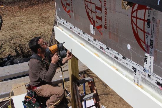 Pollard nails fascia to &frac34;-inch strapping applied over the foil-faced rigid insulation. Trim elements are spaced off the foil faced polyiso foam to facilitate the drainage of wind driven water and drying of the wood trim. The beam trim shown here is unusual, Pollard points out: it is the only trim or siding element on the building exterior where the space behind the trim has no air inlet at the bottom or exhaust at the top for air to flow freely. However, the air space behind the wood trim, combined with a coat of primer and first coat of paint, should still add to service life of the wood and the paint job.