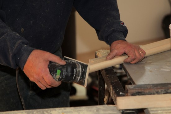 A vibrating sander smooths the round-over cut on the ends of the stool.