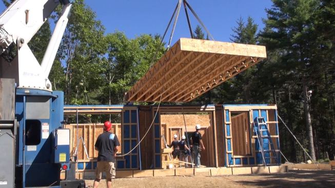 With all the walls set, plumbed, anchored, and braced, the crew starts to crane floor sections into position. A crew member tethers the panel with a rope to help guide it and prevent spinnng.