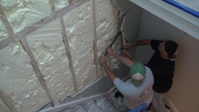 The objective: Prevent unwanted sound from entering the apartment from the unit next door through the shared party wall in the stairwell. The crew starts by protecting the existing finished wood stair treads with cardboard, paper, and tape, then proceeds to remove the drywall from the party wall.