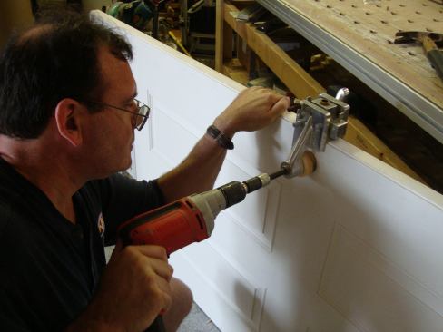 After clamping the jig in position, Greg drills the hole for the lockset using a heavy-duty 1/2-inch drill. The 2 1/8-inch drill bit is part of the jig.