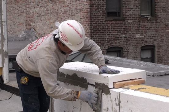 A carpenter from J’s Custom Contracting applies mortar to the joints between EPS foam insulation pieces for the exterior insulation finish system (EIFS) cladding on the masonry parapet.