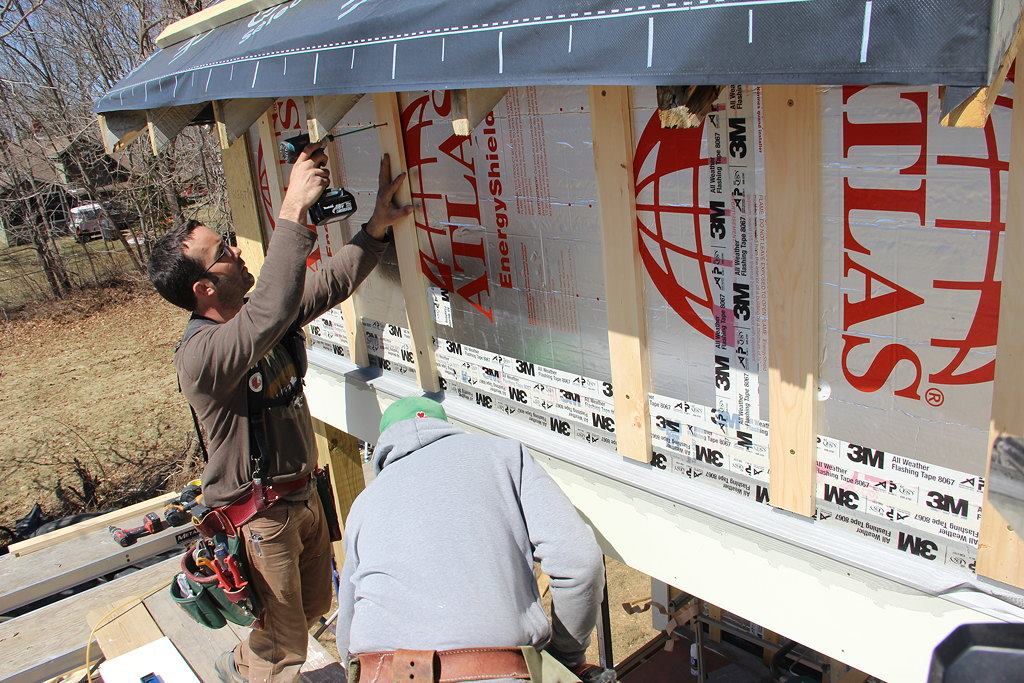 A look at the mostly furred-out wall shows the key durability details of the rain screen system: the foil drainage plane sealed with tape, the furring which creates an air space for drainage and ventilation, and the flashing and bug barrier at the bottom which will allow inflow of air into the cavity, equalizing air pressure across the siding and permitting incidental water to drain out of the assembly.