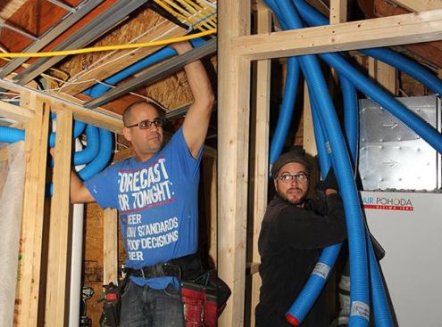 In this split image, Diego Gutierrez and Travis Anderson work together to run tubing from supply registers back to the Air Pohoda ERV core and air handler. At the air handler, Anderson labels each line to identify the location it serves at the other end. This aids in balancing the system when the house is commissioned.