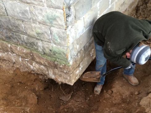Mason Joe Martignetti hand-digs under the corner of the block foundation wall to start the underpinning work.
