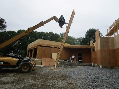 A four-wheel-drive all-terrain forklift lifts a wood I-joist rafter up to the framers.