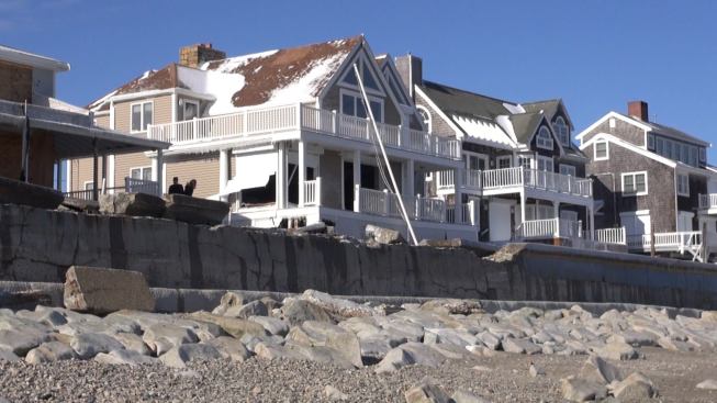 A view of the damaged Marshfield seawall from the beach below. At high tide during the storm, waves overtopped the seawall and tore chunks of concrete from its cap. Crashing surf reached as high as the roof ridges of these buildings, eyewitnesses say. The house at center was severely damaged, with water crashing through the front windows and doors and continuing through the house to blow out windows on the landward side of the building.