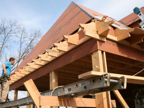 We made a template out of salvaged eaves material for the applied eaves that would not only match the soffit, fascia, and crown molding on the existing house, but would also match the concave flare in the roof plane. Working on site, we used the template and a jigsaw to cut profiles from 2x12s. We laid out the applied eaves at 16 inches on-center—using a 2x4 ledger to keep everything in line—and fastened them off with 10d commons, eight per tail.