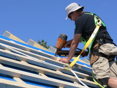 Using a spacer block, a carpenter applies more courses of 2x4 cross-strapping to the roof.