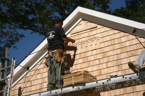 The siding contrator finishes shingling the gable above a decorative shingle version of the international H4H logo that the homeowner had prepared beforehand.