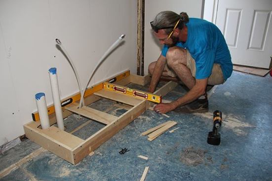 After scribing and cutting the back of the box to conform to the irregular floor, Jeff shims the front of the box to create a perfectly level base for the cabinet.