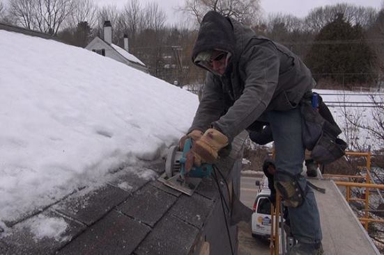 EcoCor job foreman Dan Armstrong rips through the house’s existing roof sheathing and asphalt shingles. The roof will be cut back to the plane of the wall below, and an air-tight vapor control membrane will be applied to the existing wall sheathing below and integrated into the roof air barrier and drainage plane (a layer of ice and water shield). The wall and roof will then form a continuous air-tight shell around the house. Outboard of the wall membrane, the crew will apply an insulated assembly of wood I-joists and cellulose insulation.