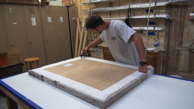A crew member wraps the screen-printed panel cover around the back of the panel and staples it to the panel frame and back. Steve Drago, son of company founder Joseph Drago, sometimes has to tweak the screen-printing source images with PhotoShop software in order to make the images wrap appropriately around the two-inch-thick panel frame edges.