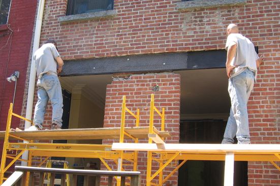 Plans call for the header assembly to be finished with stucco, so workers flash it with felt paper and fasten galvanized steel mesh to it as they bolt the two channel sections together.