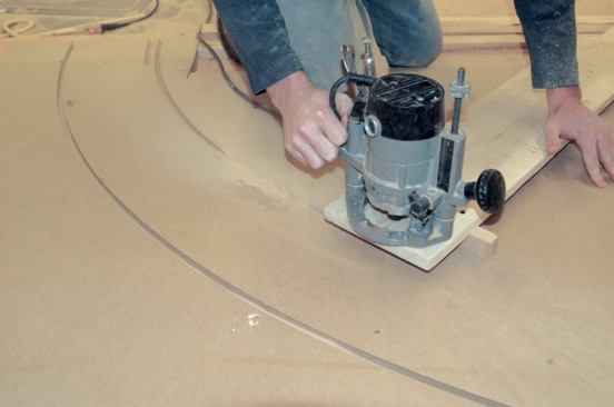 A block of wood screwed to the end of the trammel supports the router above the work.