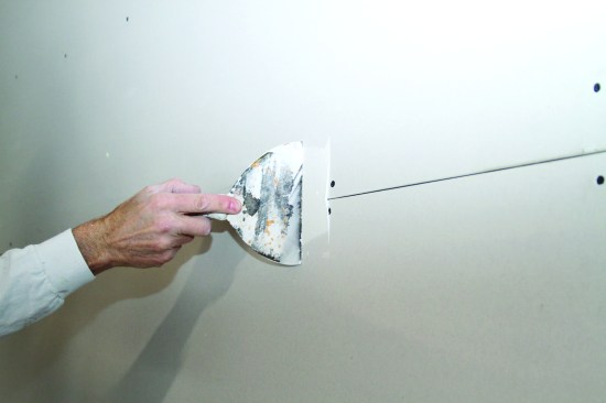 The author uses a 6-inch knife for the first coat, applying a healthy 1/8-inch-thick bed of compound on the seam.