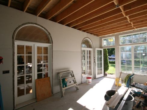 After the rough wiring was completed in the sunroom, we insulated the knee walls, the open space in the posts, and the stud bays of the gable-end wall of the existing house with “Thermoseal” open-cell spray foam (hitting the gaps at the windows with low-expanding foam). We sprayed the whole roof assembly as well, leaving the sunroom’s ceiling uninsulated. After hanging &frac12;-inch drywall on the posts and all of the walls, we converted the two exterior doors in the existing gable-end wall into interior doors. This involved removing existing weatherstripping and the exterior sills