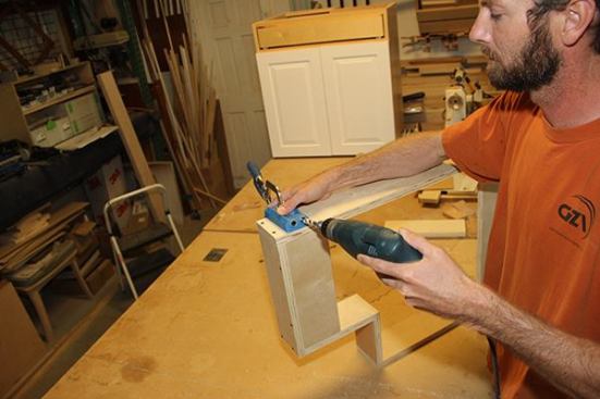 As a final step, Jeff uses a small clamp-on jig as a drill guide for making pocket holes in the toe-kick base. On site, he’ll set screws into the pockets to secure the toe kick to the kitchen floor.